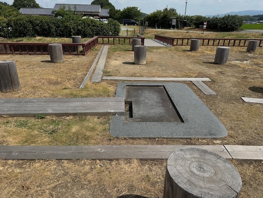 遺構の中央。灰色の台に黒い長方形のくぼみ、漏刻の座。周りに柱位置の切り株。